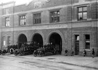 South Wellington Fire Station on the corner of Constable Street and Alexandria Street, Wellington. Shows three fire trucks occupied by firemen in uniform. A few children look on. Photograph taken by Sydney Charles Smith 1922