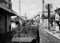 Army trucks of the New Zealand Medical Corps, 6NZ Fd Amb, driving through a street in Larissa, Greece. Taken by A H Thomas, 18 April 1941