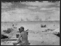 Enemy shells bursting on a ridge in the south sector, El Alamein, Egypt, near the positions of New Zealand soldiers in 27 Battery, 5 Field Regiment. Shows an unidentified soldier in the foreground. Photograph taken by J C Pattle.