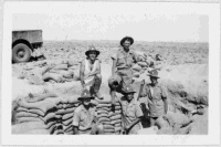 Five members of the 27 New Zealand (Machine Gun) Battalion beside sand-bags on the edge of a gun position pit during the training days in Egypt, 1940. Photograph taken by W R Norman.