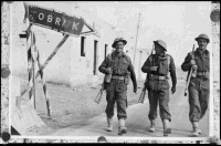 Three unidentified New Zealand soldiers on the Derna Road in Tobruk during the advance into Libya, during World War 2. Shows three soldiers walking past a 