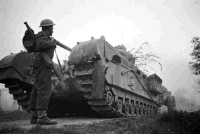 NZ soldier and Churchill Crocodile tank at dusk, as the attack goes in on the Senio River defences. Photograph taken in Italy by George Kaye on the 9th of April, 1945.