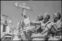 New Zealanders along the New Zealand Division Axis sign set up in the town of Atina, Italy. Shows C Bills (Otaki), J L Milne (Lower Hutt), and J Franklin (Christchurch), looking at a sign-post that points in one direction to 