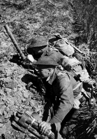 Two New Zealand soldiers of the 26th Battalion in a slit trench in the Senio area, Italy, during World War II. They are waiting for the word to advance while the battle continues just over 1000 yards away. Nearest the camera are D E Hale (Blenheim) and J Russell (Chch).  Photograph taken by George Kaye, 10 April 1945.