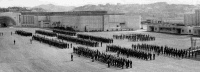 Rows of uniformed Royal New Zealand Air Force members standing in front of the New Zealand Centennial Exhibition buildings, Rongotai, Wellington. Photograph taken in 1942.  Historical Notes: The RNZAF set up a Recruiting Centre and an intitial training school for pilots, observers and air gunners in the old Centennial Exhibition buildings in September 1939. By 1940 the buildings also housed the Technical Training School.