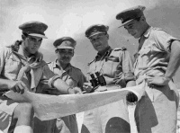 Behind the El Alamein front, on the eve of the successful offensive which commenced on Oct 23, a group of Maori officers study a map of the Western Desert. From left to right: Lt G Marden (Nth Ak), Lt J Aperahama (Nth Ak), Capt JC Henare (Nth Ak), Capt W Porter, [MC, Bar] (Nth Ak).  Photograph taken by M D Elias.